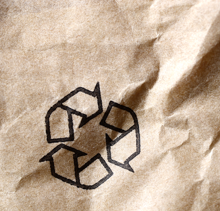 A close-up of a black recycling symbol printed on a crumpled brown paper bag.