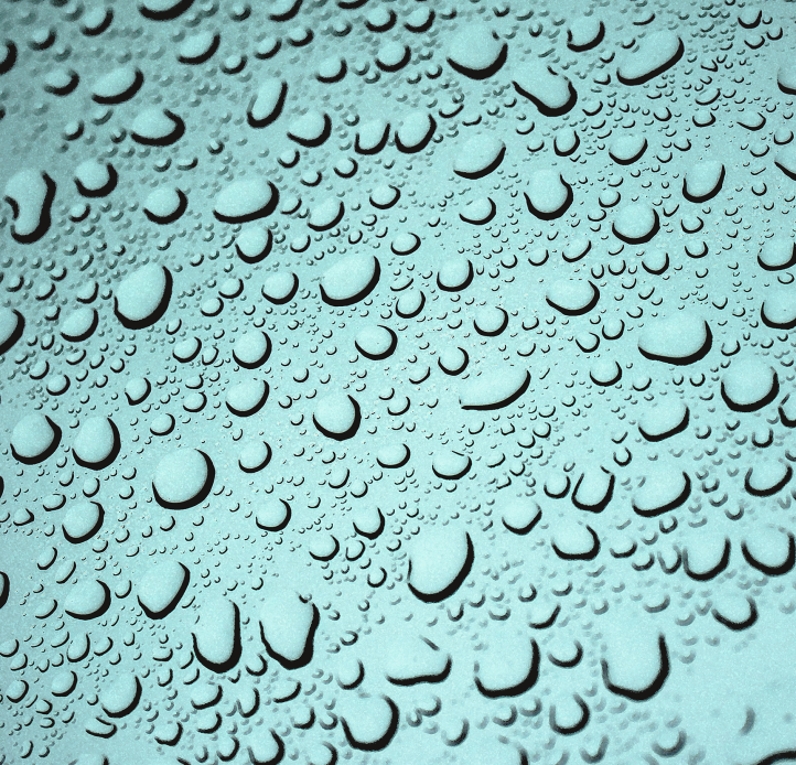 A close-up shot of numerous water droplets of varying sizes clinging to a textured, light blue surface.