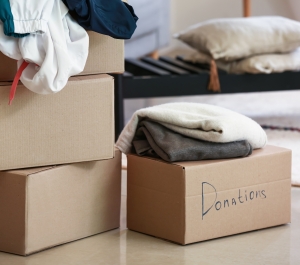 Moving boxes, one labeled "Donations," are filled with clothes on a floor.