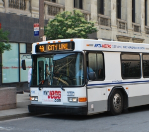  A white NFTA-Metro bus with "4A CITY LINE" displayed on its marquee is parked on a city street in front of historic buildings.